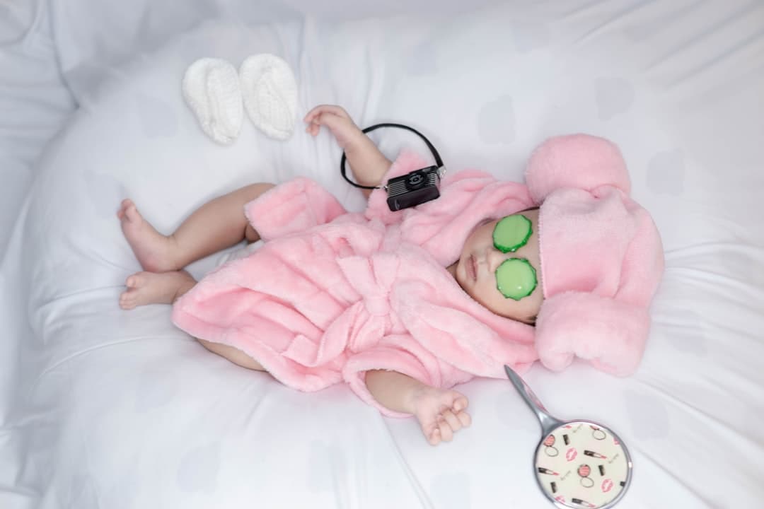 A baby girl in a pink dress laying on a bed