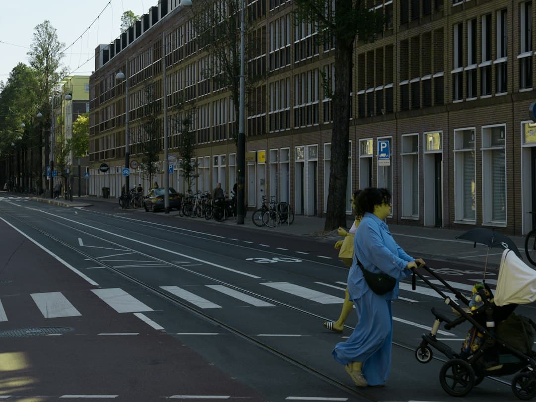A person in a blue outfit pushing a stroller across a city street